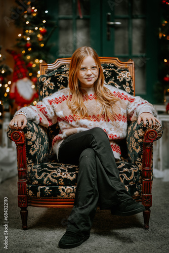Young teenager girl sit on the chair near decorated Christmas tree. Season greetings © Raivo
