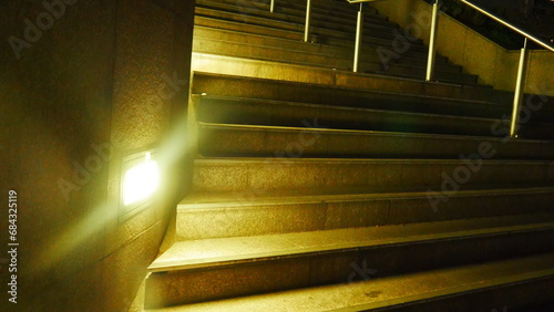 Grand plan d'escalier éclairé par des projecteurs de lumière blanche ou jaune, vide, construction urbaine et taillé dans la roche, peu d'éclairage, longue marche, solitude, silence, monté ou descente