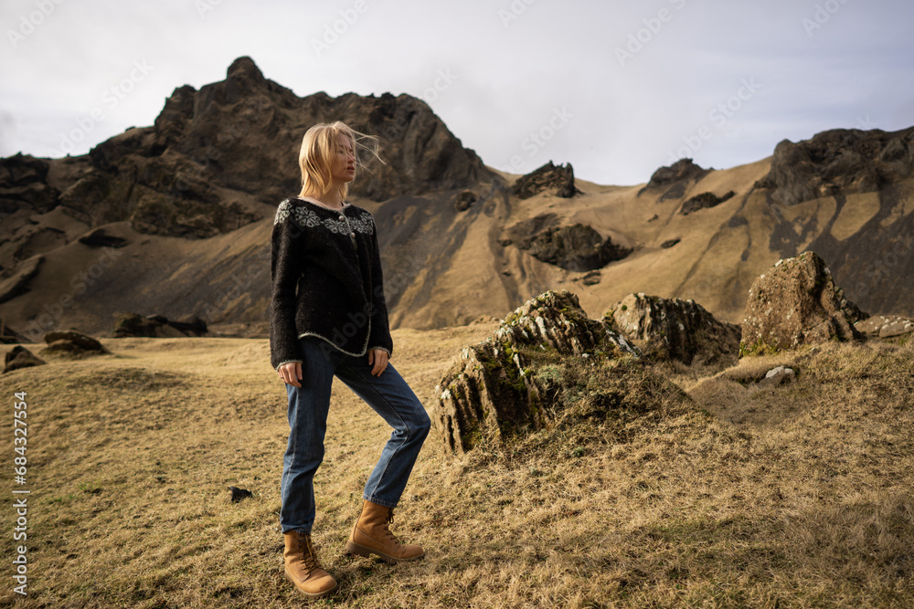 A girl in fashion clothes poses in mountains an Icelandic sweater