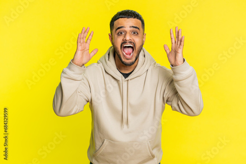 Irritated angry Indian man screams from stress tension problems feels horror hopelessness fear surprise shock expresses rage nervous, quarrel. Arabian young guy isolated on yellow studio background