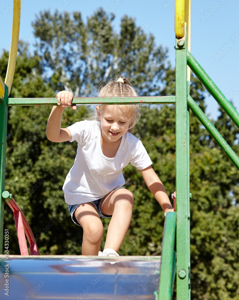 Obraz premium Little girl playing on a slide in a playground in the summer city park. Childhood, leisure and people concept - happy child rest and have a good time