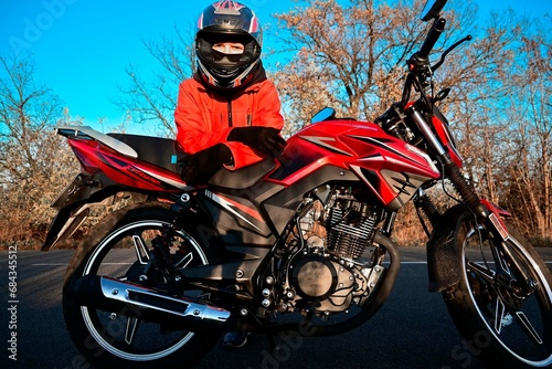 young attractive biker girl in red sitting next to her red motorcycle in the middle of the road. biker with a motorcycle outside the city.