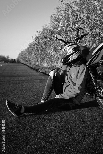 young attractive biker girl in red sitting next to her red motorcycle in the middle of the road. biker with a motorcycle outside the city.