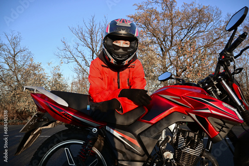 young attractive biker girl in red sitting next to her red motorcycle in the middle of the road. biker with a motorcycle outside the city.