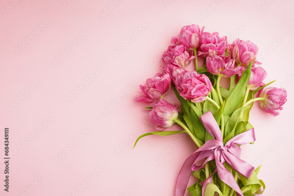 Bouquet of pink peony tulips tied with a pink bow. Spring flowers on the pastel pink background and place for text. Festive concept for Valentines Day or Mother's Day.
