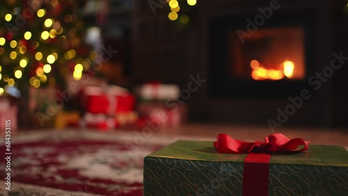 Green gift box in classical Christmas decorated interior living room library with fireplace. Christmas gift near fir tree on Christmas eve. Modern classic style interior design apartment. Christmas photo