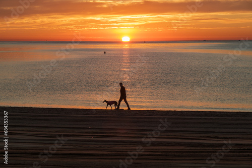 Málaga, playa MIsericordia, amanecer sobre el mar, primeros rayos del día, hombre paseando por la orilla con su perro, tranquilidad y felicidad photo