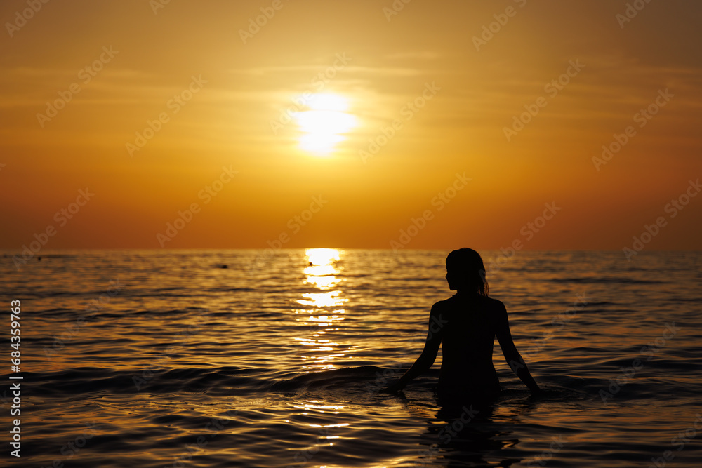 Silhouette of a girl standing in the sea at sunset.
