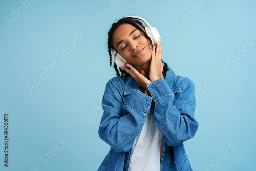 Happy African American woman wearing denim shirt with closed eyes listening to music in headphones photo