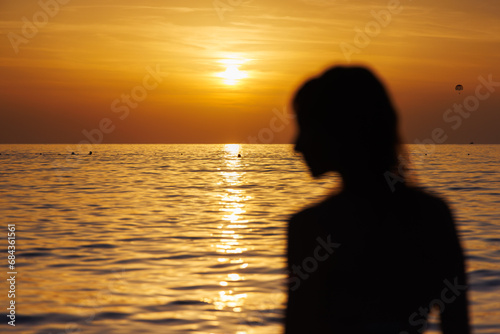 Silhouette of a girl's profile in out of focus against the background of the sea at sunset. © Yurgentum