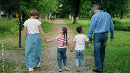 Mom, dad, child, big family. Happy family with three children walks outdoors in city park in summer. Parents children go together, family weekend. Family holiday. People walk in park holding hands. © zoteva87