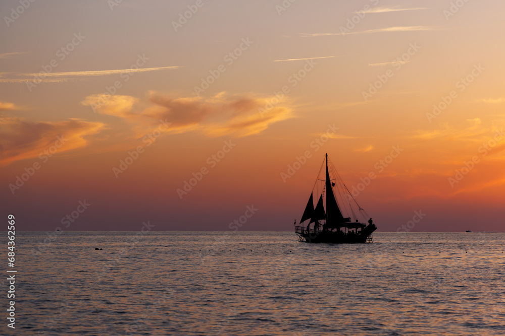 Silhouette of a sailing ship at sunset under the magestic sky.