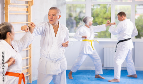 Elderly women and men in pairs exercising karate movements during group training