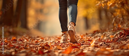 Female legs in hiking shoes walking through autumn leaves on forest path