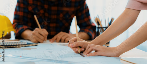 Cropped image of cooperative architect team decide and work together on meeting table with house model, safety helmet and architectural plan scatter around. Closeup. Focus on hand. Burgeoning. photo