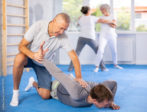 Senior man train in pair with middle-aged coach to strike and reflect blows of enemy. Intense moment as two individuals engage in self-defense training, showcasing skill, reaction, repulse