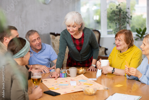 Happy elderly woman playing board game with group of friends at table. Concept of socialization of older adults
