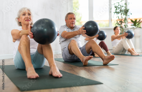 Portrait of mature people doing exercises for press with pilates ball during group class in fitness studio