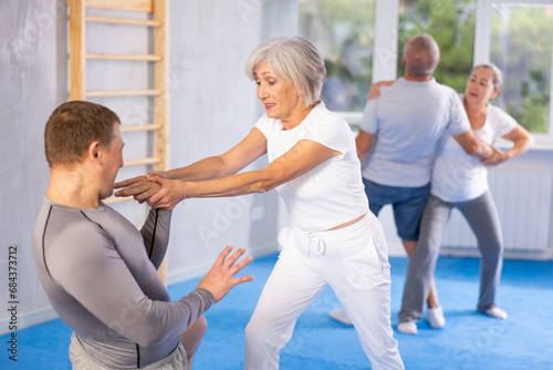 Elderly woman twists the arm of attacking man with painful hold in gym. Self-defense lesson © JackF