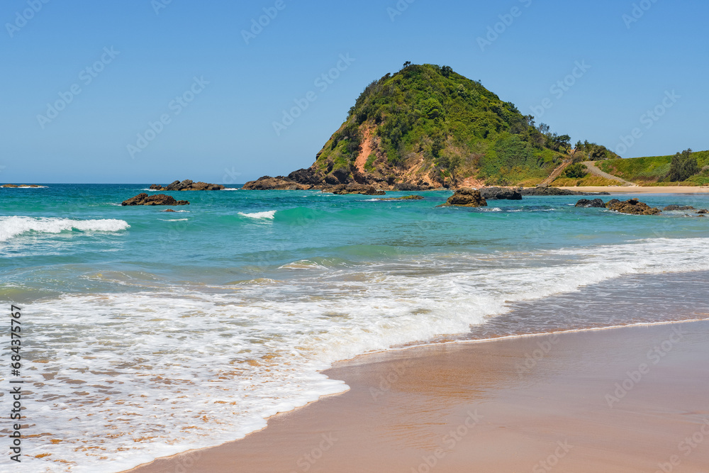 Australian coast, big rock on the seashore with blue water with waves and sandy beach, view from the beach to the seaside landscape on a summer sunny day.