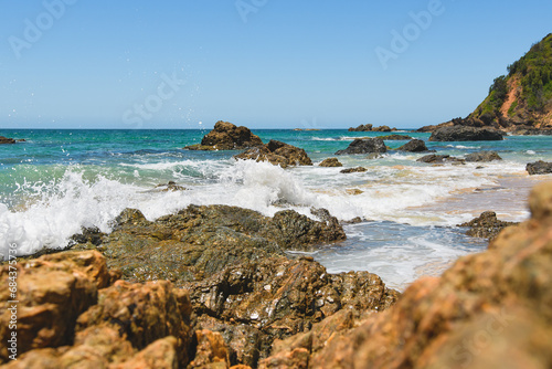 Australian coast with volcanic rocks at the shore, view from the beach to the horizon with blue water with waves on a summer sunny day.