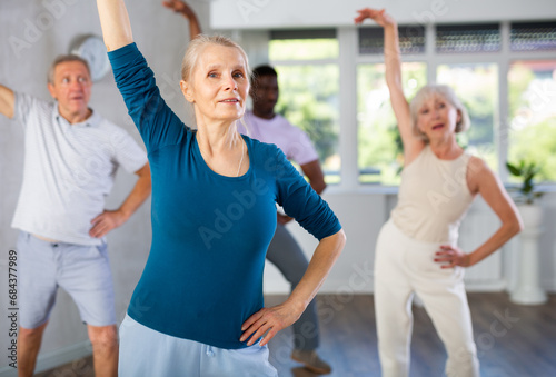 Enthusiastic elderly woman practicing modern vigorous dance movements in group dance class for adults