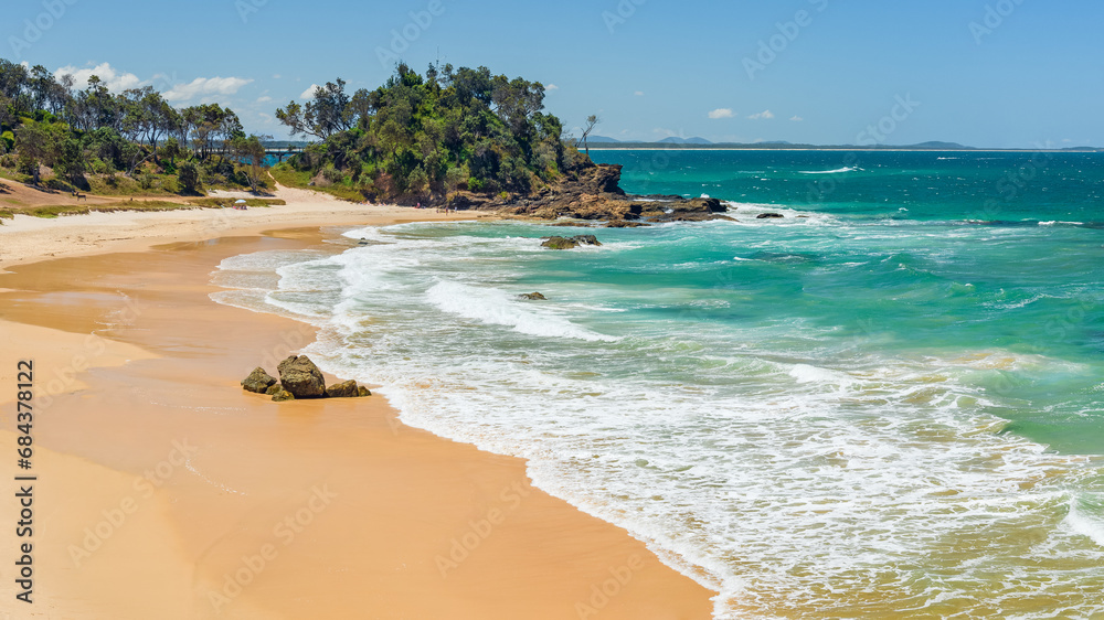 Australian coast, view from a cliff of a sandy beach with a rocky shore and blue water on a sunny day. Sea landscape on a warm summer day.