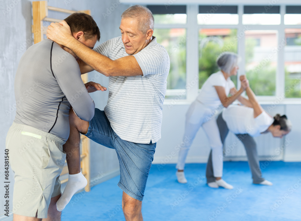 Obraz premium Mature man at a self-defense lesson learns how to make painful blows with his hand and foot