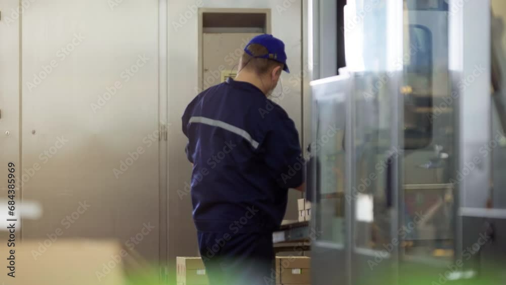 Milk Production Plant. Male Worker is Waiting at the End of the Conveyor line. Collecting the Cardboard Package with Small Green Packets inside of the box. Industrial Factory. Packaging Process. Milk Production Plant. Male Worker is Waiting at the End of the Conveyor line. Collecting the Cardboard Package with Small Green Packets inside of the box. Industrial Factory. Packaging Process.