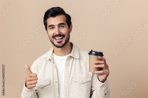 Portrait of a stylish man with a glass of coffee with himself mockup on a beige background in a white t-shirt, fashionable clothing style, space space