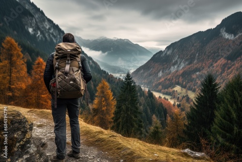 A hiker with a large backpack on a mountain path with dramatic peaks in the background and autumn-colored grass in the foreground © InfiniteStudio