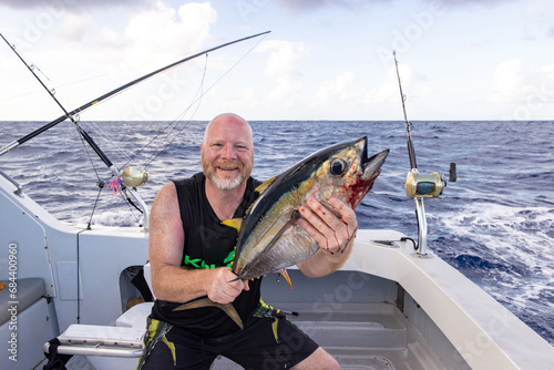 Happy man holding a fresh caught bigeye tuna fish on a small charter boat in Hawaii.  photo