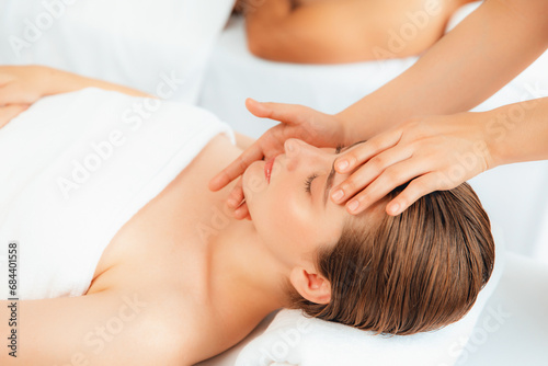 Caucasian couple enjoying relaxing anti-stress head massage and pampering facial beauty skin recreation leisure in dayspa modern light ambient at luxury resort or hotel spa salon. Quiescent