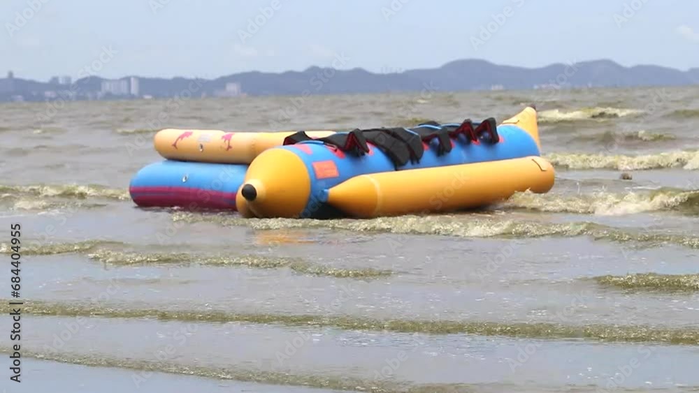 Empty yellow banana boat floats in green sea on beach, moving with wind and waves. Rides that are available to tourists. Green dark sea water wave natural phenomenon. Seawater in Bang Saen, Chonburi Empty yellow banana boat floats in green sea on beach, moving with wind and waves. Rides that are available to tourists. Green dark sea water wave natural phenomenon. Seawater in Bang Saen, Chonburi