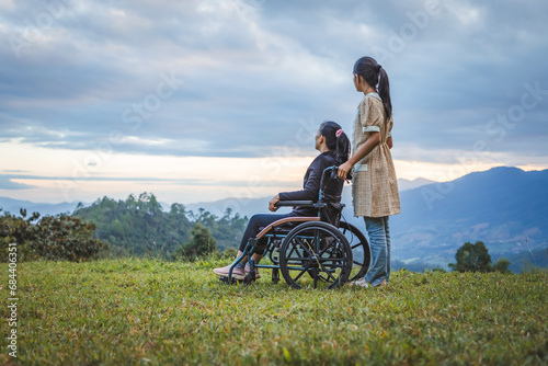 Happy young mother in wheelchair with care helper daughter in spring nature at sunset.
