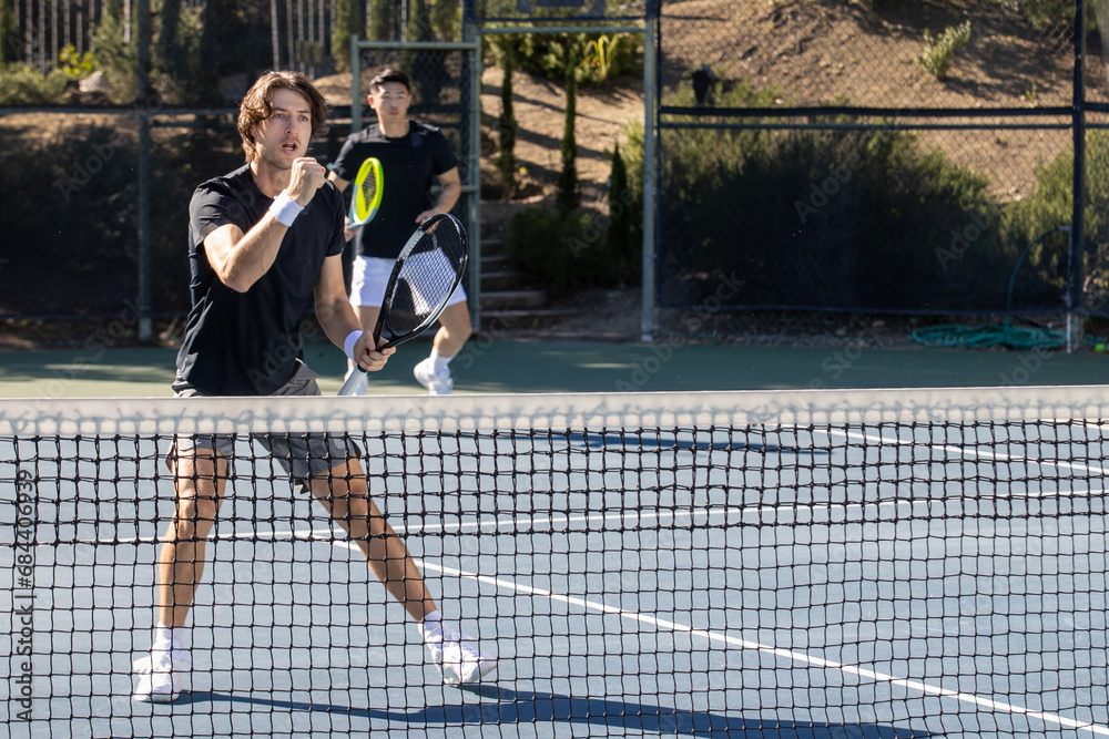 Two adult men playing an intense game of tennis together on an outdoor court. The sport is fast and they are training during practice. 