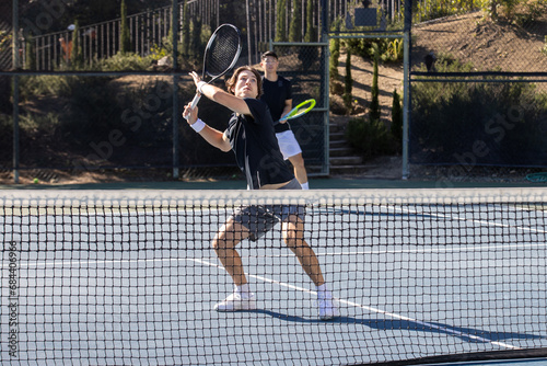 Two adult men playing an intense game of tennis together on an outdoor court. The sport is fast and they are training during practice. 