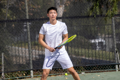 Physically fit Asian man playing tennis. The player is outside on a court with a racket during a match.