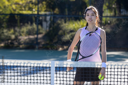 Young female Asian tennis player outside on the court playing a game. The woman is athletic and healthy. Physical fitness is part of her active lifestyle.