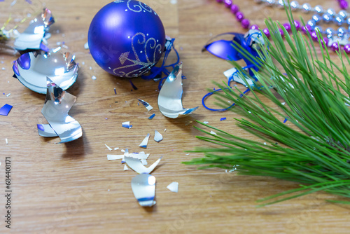 Broken Christmas tree decorations litter floor after holiday party fragments of blue New Year ball, a holiday decoration on a wooden laminate next to a green branch Sharp shards of broken glass toys