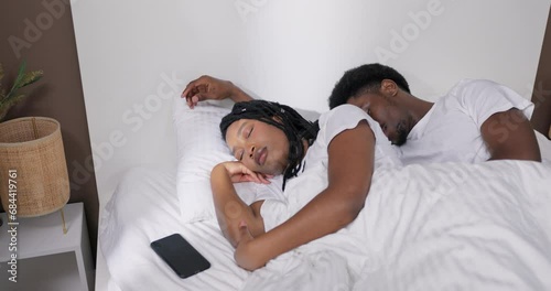 Curious young african american dark skinned man sleeping with her beautifuladorable wife in bed taking her cell phone in the middle of rhe night checking all sms messages not trusting her woman. photo