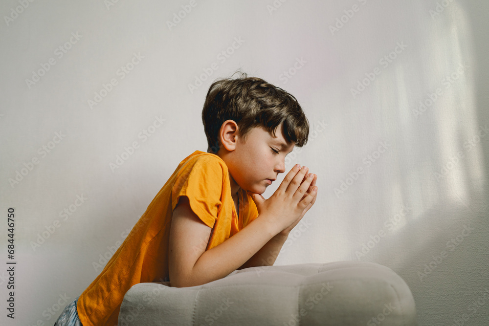 Obraz premium A boy in an orange T-shirt prays at home. Reading the Holy Bible. Concept for faith, spirituality and religion. Peace, hope.