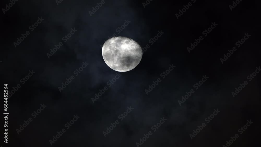 Bright white moon craters and ridges rises in sky as clouds pass below at night Bright white moon craters and ridges rises in sky as clouds pass below at night