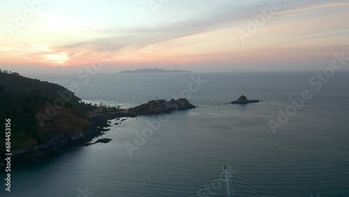 Sunrise over a rocky headlnad sporting a white lighthouse. A boat below heads for the rocky outcrop and island. Koh Lanta national parkl photo