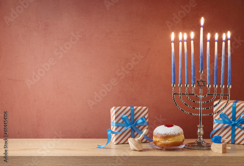 Jewish holiday Hanukkah background with menorah, traditional donuts and gift box on wooden table