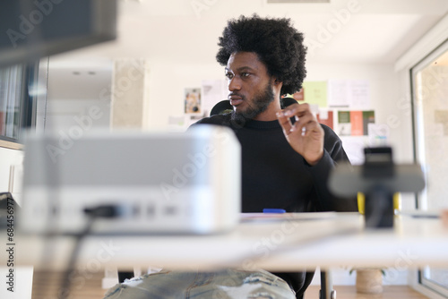 In the office. Relaxed worker sitting comfortably at his desk working with his computer. He dresses casually, is bearded and has an afro look. photo