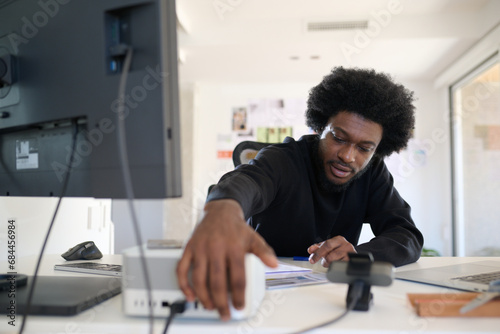Turning on the computer. Turned off the computer. Man in the office with afro hair leans over his computer to turn it off or on photo