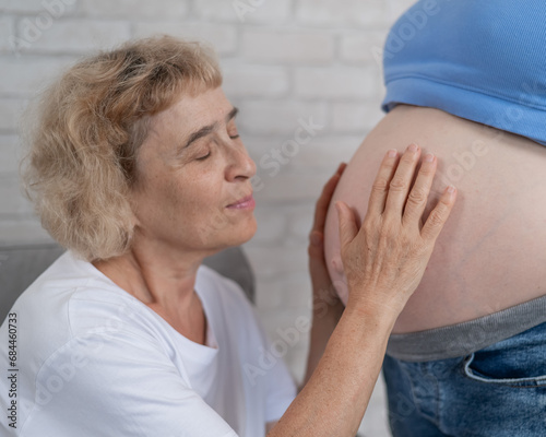 An elderly woman leans against the belly of her pregnant daughter. Close-up.