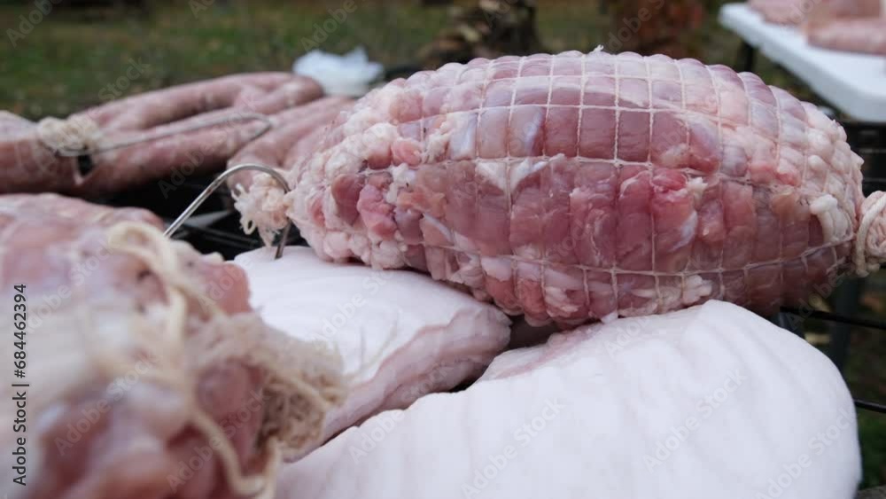Raw pork in ham sacks placed on cured pork belly next to rings of fresh stuffed sausages ready to be smoked in back yard home made smoker.