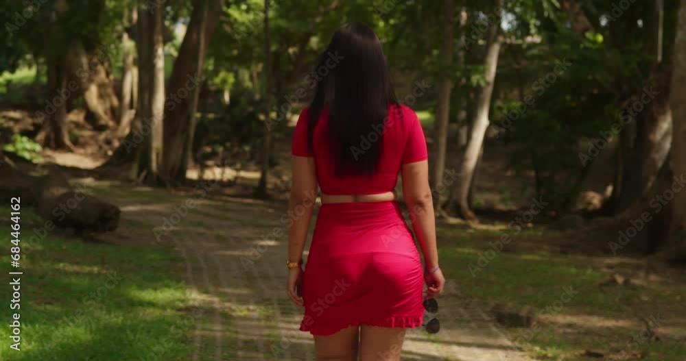 The Caribbean's vibrant park featured a woman in a captivating red dress walking on a sunny day The Caribbean's vibrant park featured a woman in a captivating red dress walking on a sunny day